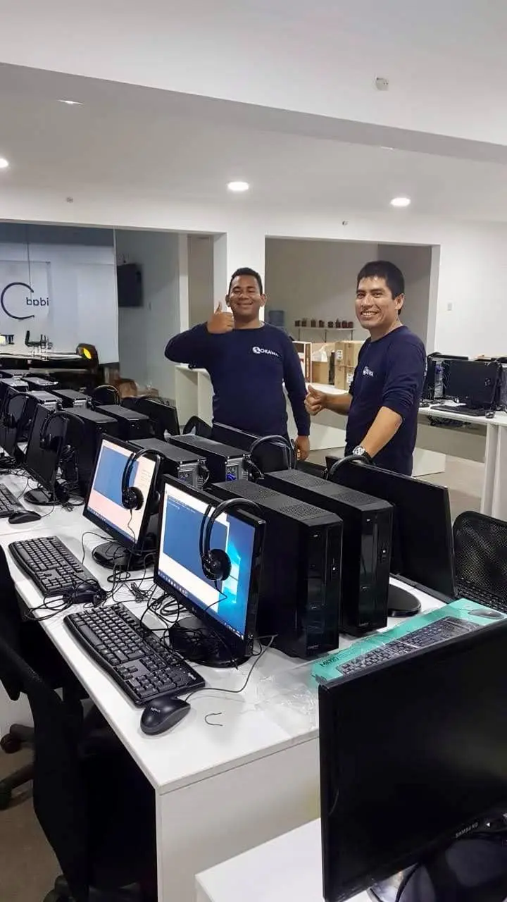 Técnicos de Okawa en un laboratorio de cómputo con varias computadoras de escritorio listas para ser usadas en un call center.