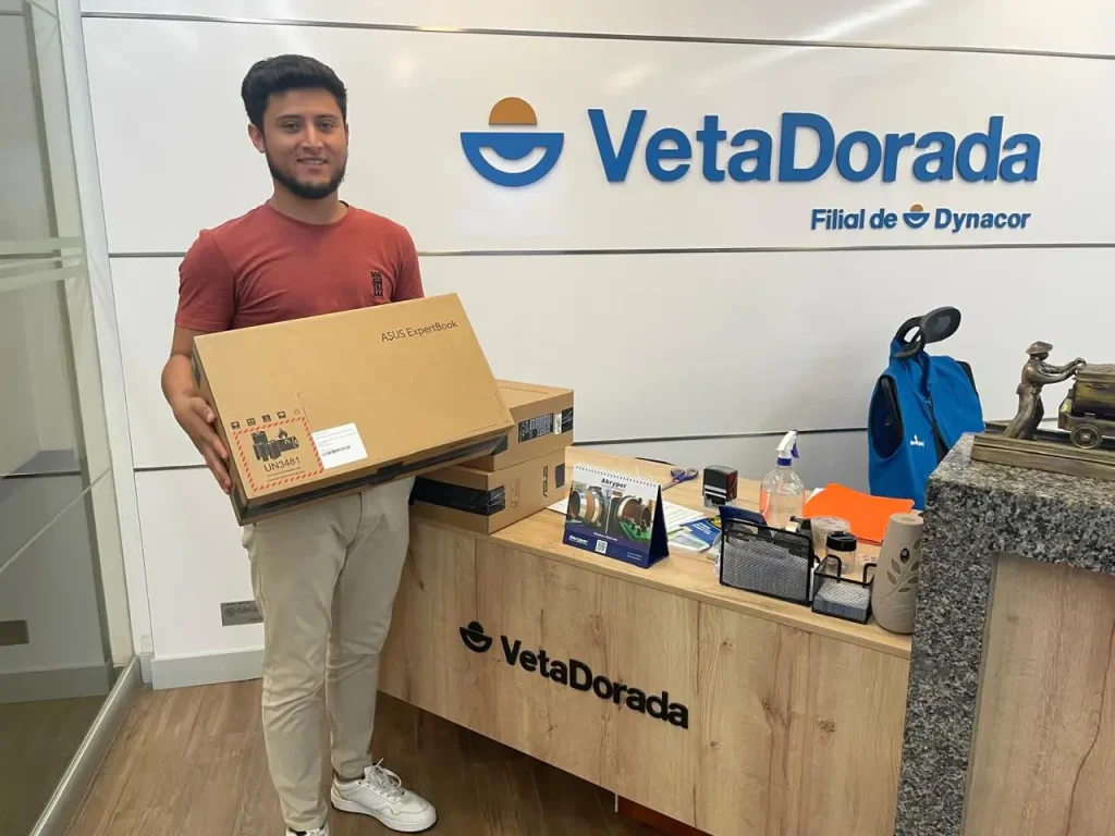 Joven sosteniendo una caja de laptop ASUS en la recepción de Veta Dorada, empresa minera.