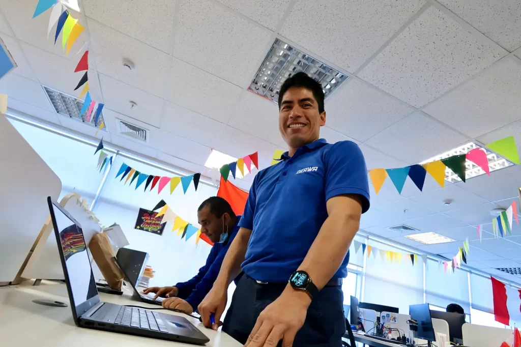 Técnico de Okawa con uniforme azul trabajando en una laptop en oficina decorada con banderines de colores.